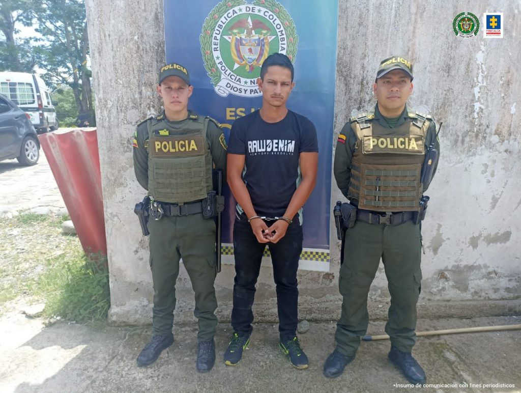 En las fotografía aparece un capturado junto a personal de Policía Nacional. En la parte posterior de la imagen se ven banners de Policía Nacional y la Fiscalía General de la Nación.