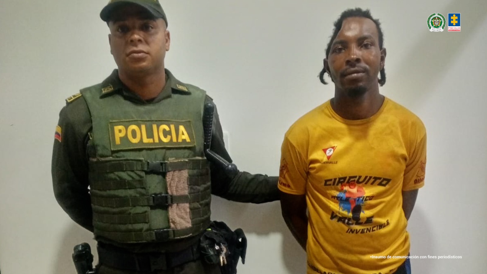 En la fotografía se aprecia de pie y con los brazos atrás a Carlos Fernando Guerrero Montaño. Viste con camiseta de manga corta, de color amarillo mostaza con estampañdo de colores. Esta persona presenta una señal particular que consiste en un hundimiento en la parte derecha de su cráneo. A su derecha hay un uniformado de la Policía Nacional.