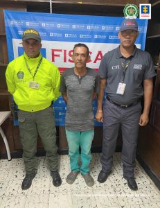 En la imagen aparece una persona, vestido con sudadera verde y una camiseta gris, entre dos uniformados de la Policía y la Fiscalía.