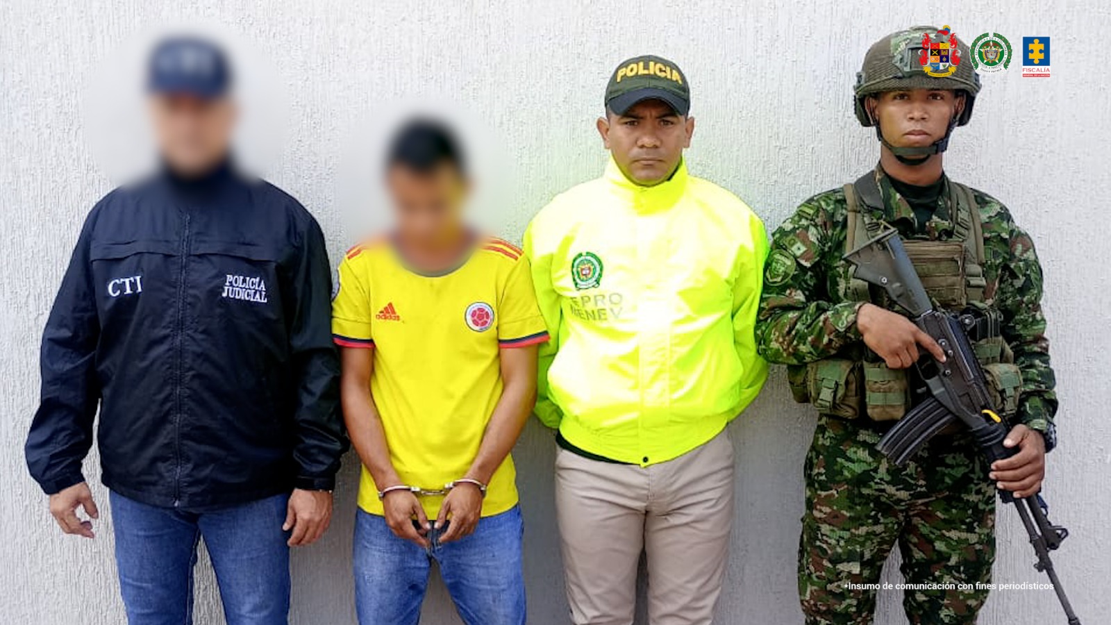El capturado se encuentra de frente y tiene una camiseta de la selección Colombia. Se encuentra custodiado por un servidor del Cuerpo Técnico de Investigación CTI, un uniformado de la Policía y Ejército Nacional.