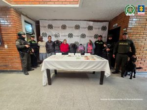  En la foto aparecen todos los capturados de frente y custodiados por uniformados de la Policía Nacional. En la foto tambien observamos parte del material incautado (estupefaciente, dinero en efectivo, grameras, empaques y marihuana). Detrás hay un backing de la Policía Nacional.