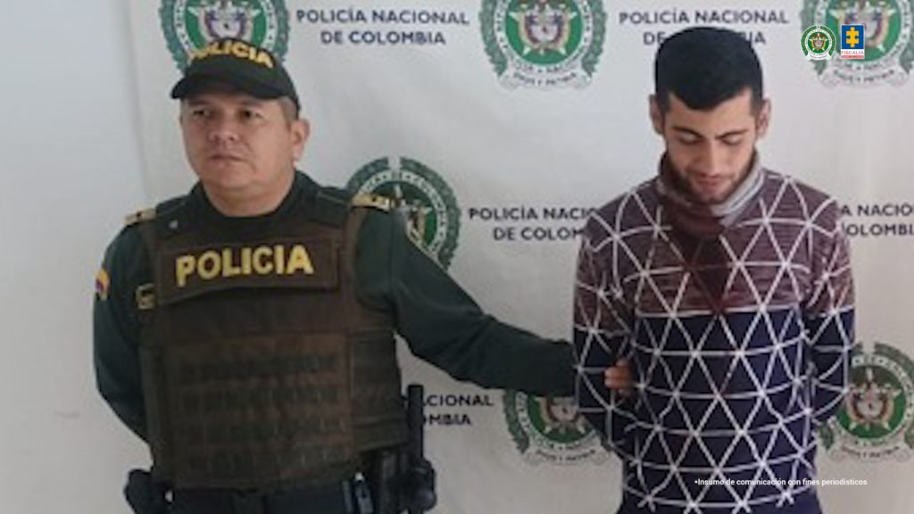 En la foto se observa al agresor en custodia por un servidor del CTI y un uniformado de la Policía Nacional. Detrás hay un backing de la Policía Nacional.