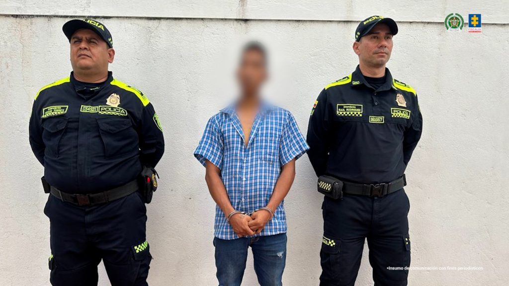 En la foto aparece el capturado custodiado por dos uniformados de la Policía Nacional. El capturado tiene una camisa azul de cuadros.