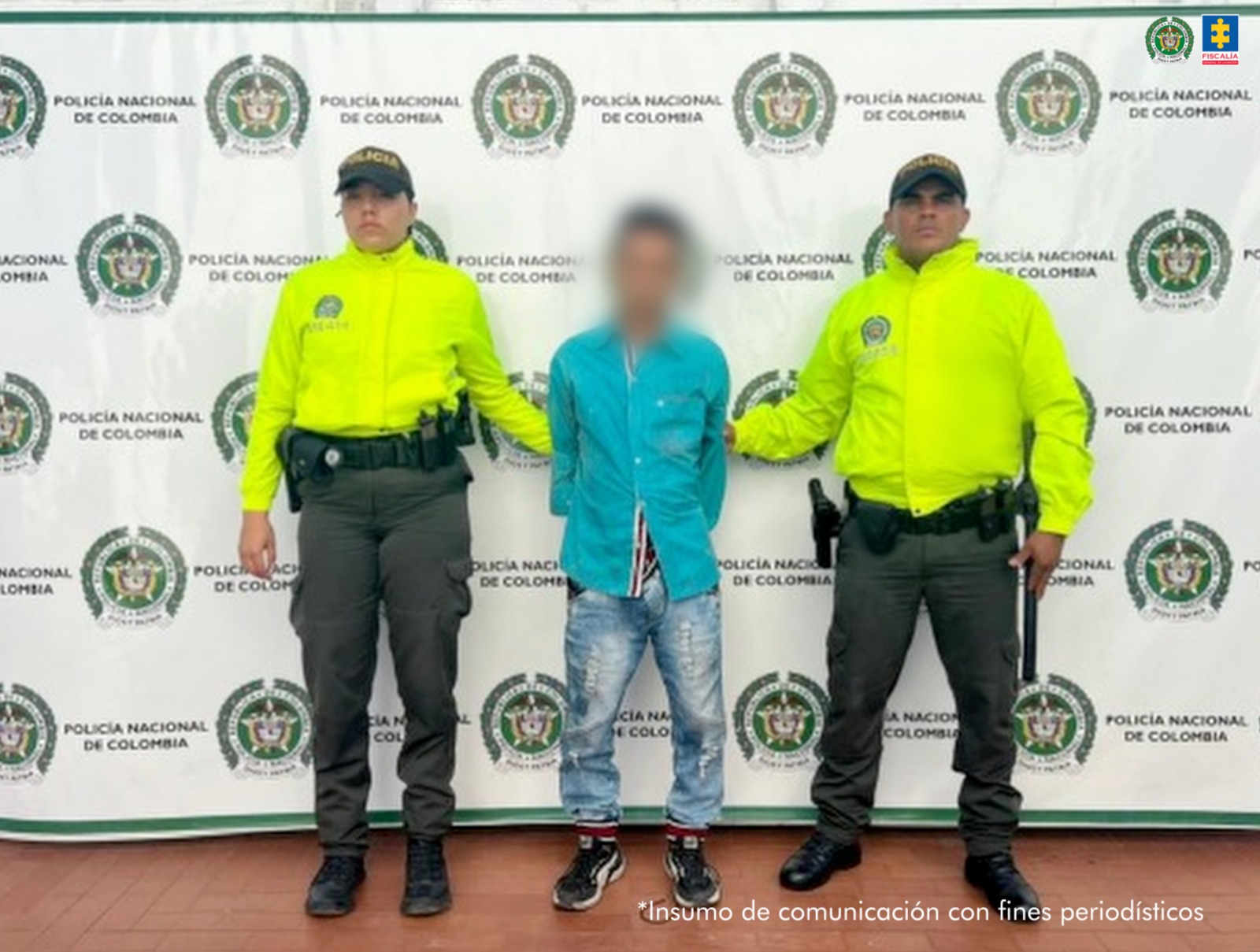 El capturado se encuentra de frente y tiene una camiseta color azul y jean. Se encuentra custodiado por dos uniformados de la Policía Nacional.