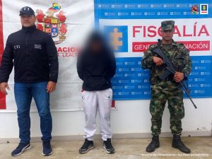En la fotografía aparece un capturado, junto a personal de Fiscalía General de la Nación y Ejército Nacional. En la parte posterior de la imagen se ven banners de Ejército Nacional y la Fiscalía General de la Nación.