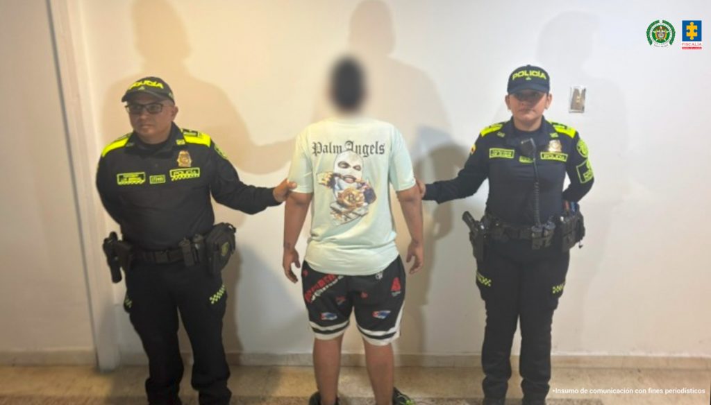 En la foto aparece el menor aprehendido de espalda y custodiado por dos uniformados de la Policía Nacional. El menor tiene puesta una bermuda con estampados.