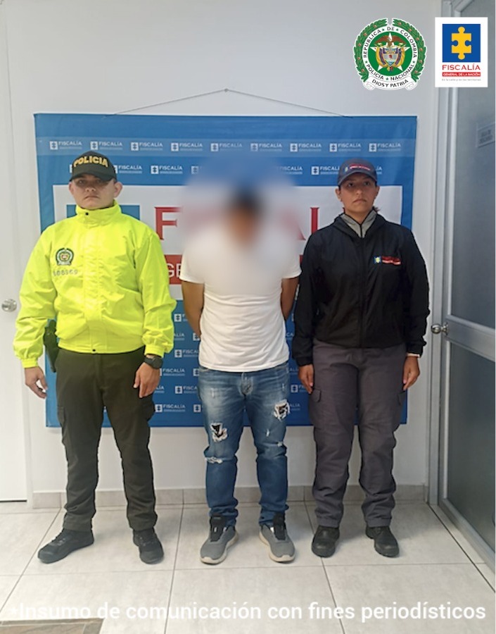 En la fotografía aparece un capturado, junto a personal de Fiscalía General de la Nación y Policía Nacional. En la parte posterior de la imagen se ven banners de Policía Nacional y la Fiscalía General de la Nación.