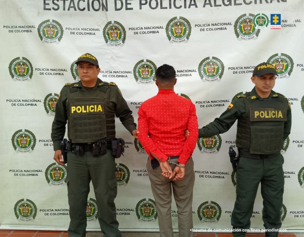 En la foto se observa al capturado de espaldas y custodiado por uniformados de la Policía Nacional. También se observa un backing de la Policía Nacional.