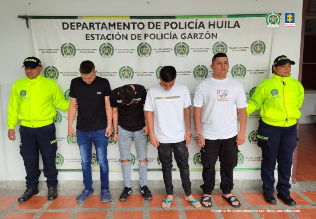 Los capturados se encuentran de frente y custodiados por uniformados de la Policía Nacional. Detrás se observa un backing de la Policía Nacional. 