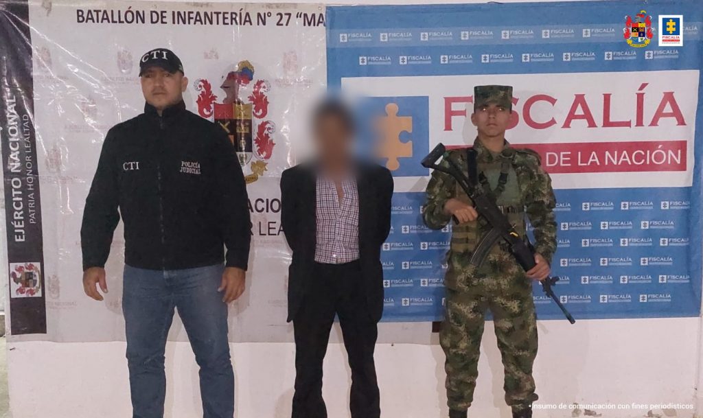 En la fotografía aparece un capturado, junto a personal de Fiscalía General de la Nación y Ejército Nacional. En la parte posterior de la imagen se ven banners de Ejército Nacional y la Fiscalía General de la Nación.