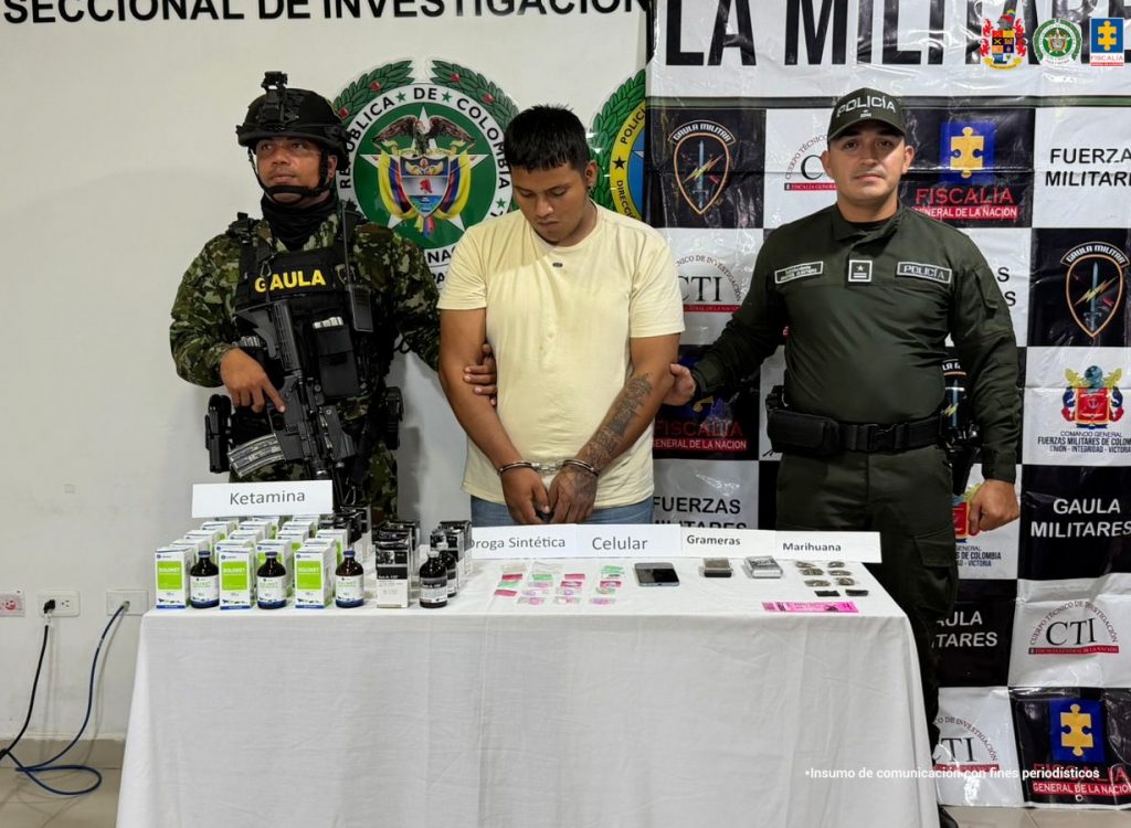 En la foto aparecen el capturado de frente y custodiados por dos uniformados de la Policía y Ejército Nacional. De fondo aparece un backing de la Policía Nacional y las sustancias estupefacientes incautadas.