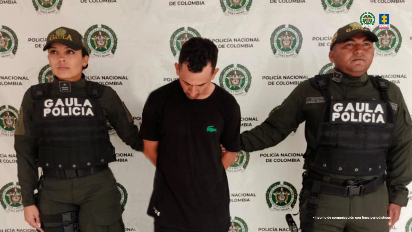 El capturado se encuentra de frente con la cabeza agachada y custodiado por dos uniformados de la Policía Nacional. En la foto se ve de fondo un backing de la Policía Nacional.