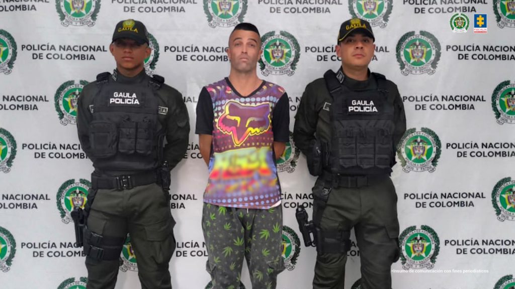 En la foto aparece el capturado custodiado por dos uniformados del Gaula Militar y de la Policía Nacional.  En la foto también aparece de fondo un backing de la Policía Nacional.