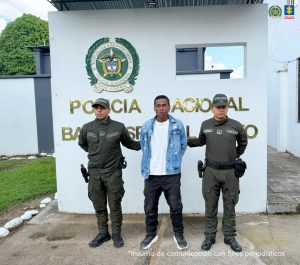 En la foto aparece el capturado de frente y custodiado por dos uniformados de la Sijin de la Policía Nacional. En la foto aparece de fondo el logo y palabras de la Policía Nacional.