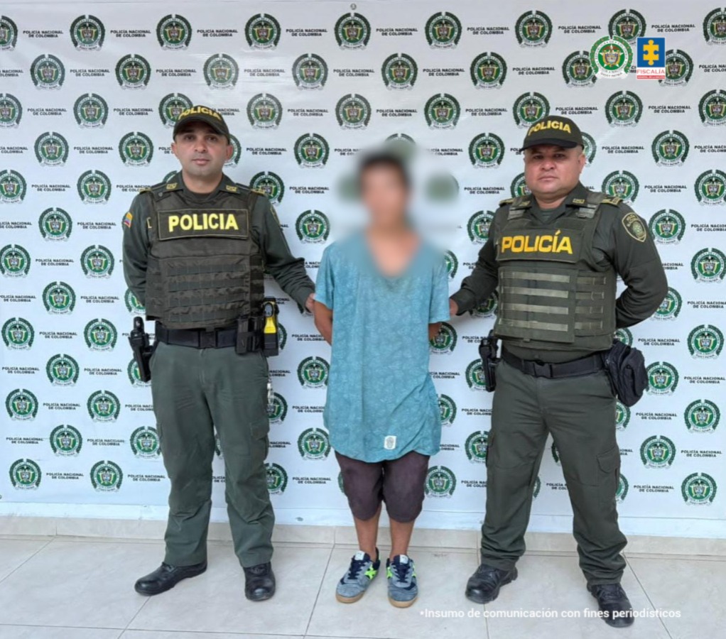 En la foto se observa al capturado custodiado por dos uniformados de la Policía Nacional. Detrás hay un backing de la Policía Nacional.