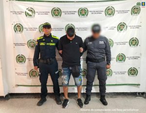 En la foto aparece el capturado de frente y custodiado por dos uniformados de la Policía Nacional. En la foto aparece de fondo un backing de la Policía Nacional.