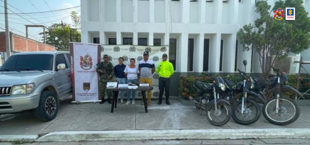 En la fotografía aparecen tres personas capturadas, dos mujeres y un hombre acompañados de dos uniformados del Ejército y la Policía Nacional. En la parte posterior hay banners con los logos de las dos entidades. 