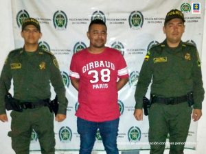 en la imagen se ve una persona detenida bajo custodia de dos policías.