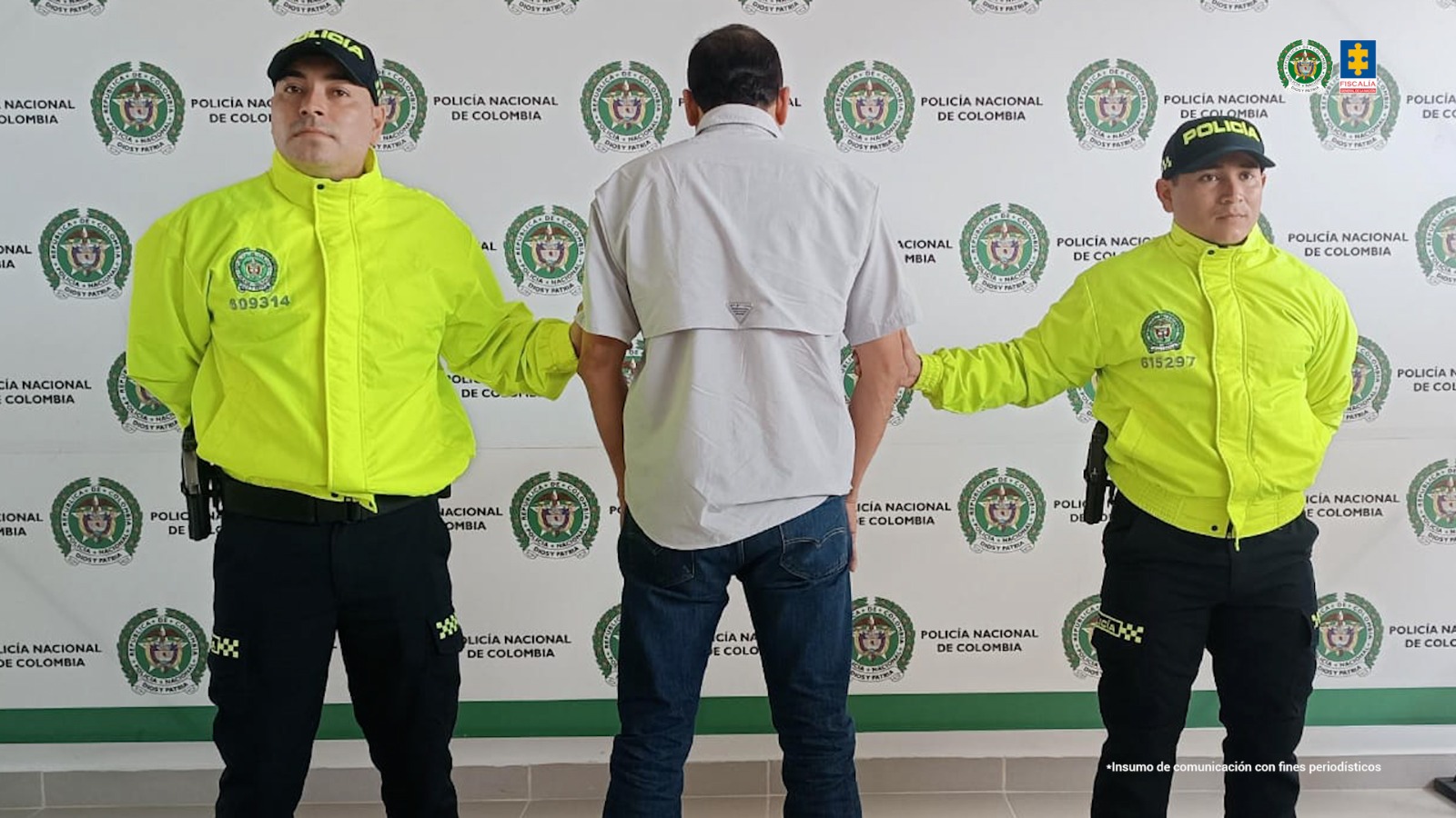 El capturado aparece de espalda a la cámara y está custodiado por dos uniformados de la policía nacional.
