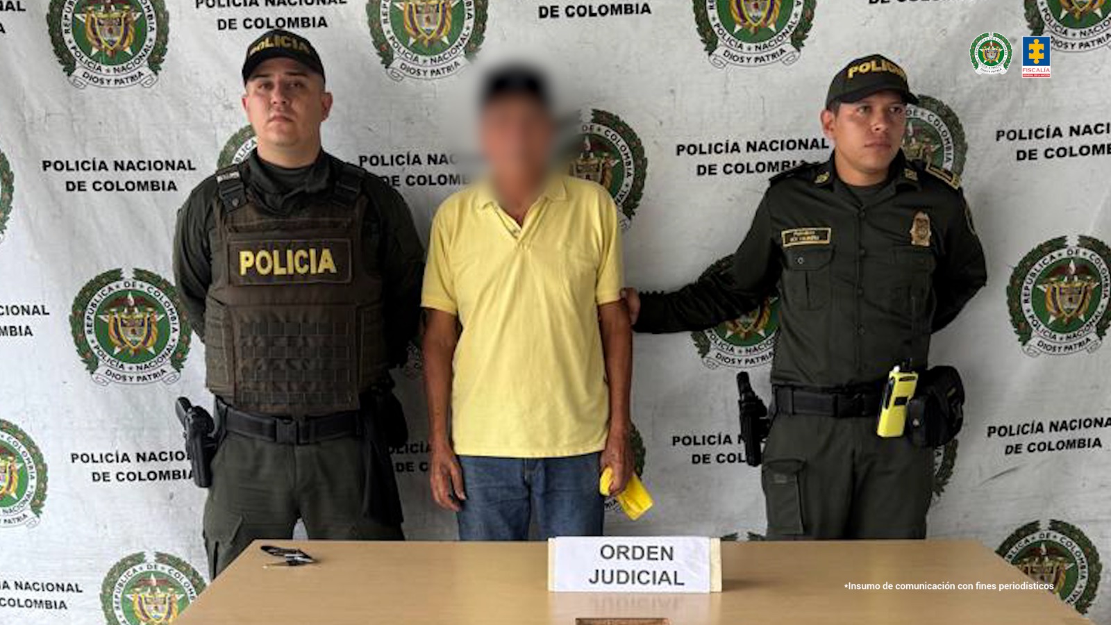 En la fotografía se aprecia de pie a César Donneys. Viste con camisa amarilla de manga corta, jean azul y zapatillas blancas. Usa gorra negra y tiene en un mano izquierda un trapo de color amarillo. A sus extremos hay uniformados de la Policía Nacional. Delante de ellos hay una mesa y sobre ella hay un letrero que dice: ‘Orden Judicial’. Detrás de ellos hay un pendón institucional de la Policía.