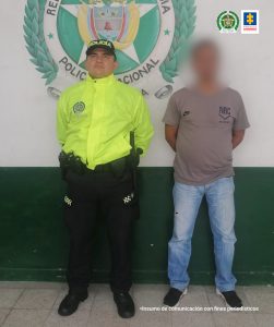 En la imagen aparece el sentenciado con el rostro distorsionado y un patrullero de la policía a su lado derecho.