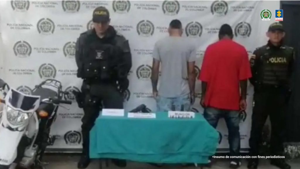 Cirilo Moreno Córdoba, alias El Negro; y a Luis Alberto Barrios Yepes, alias El Aparatoso o Sangre, acompañados a los lados de funcionarios de la Policía Nacional. A la izquierda la moto en la que huían y sobre una mesa el arma de fuego que usaron para el asesinato y las municiones.