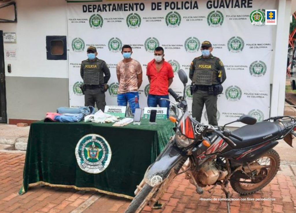 condenados de frente custodiados por dos policías uniformados, delante de ellos mesa con material incautado y detrás banner de la Policía Nacion