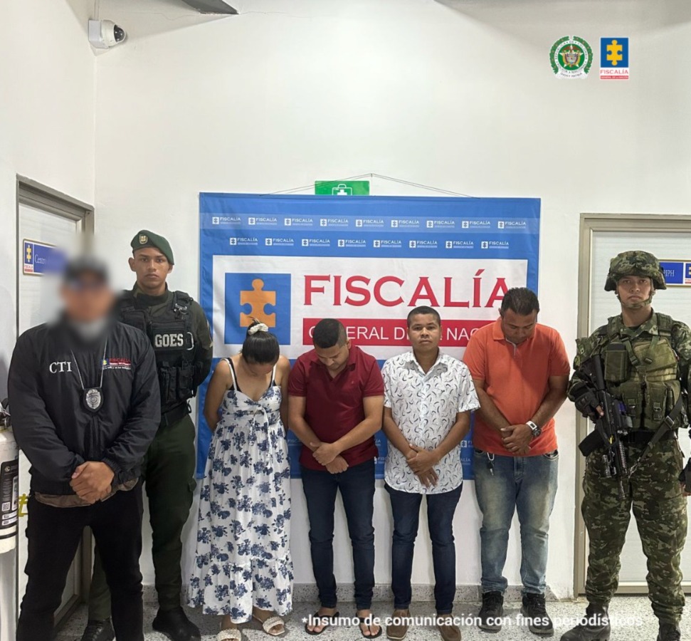 En la fotografía están los capturados de pie, tres hombres y una mujer, custodiados por uniformados del CTI y la Policía Nacional. Detrás de ellos hay un pendón de la Fiscalía General de la Nación. 