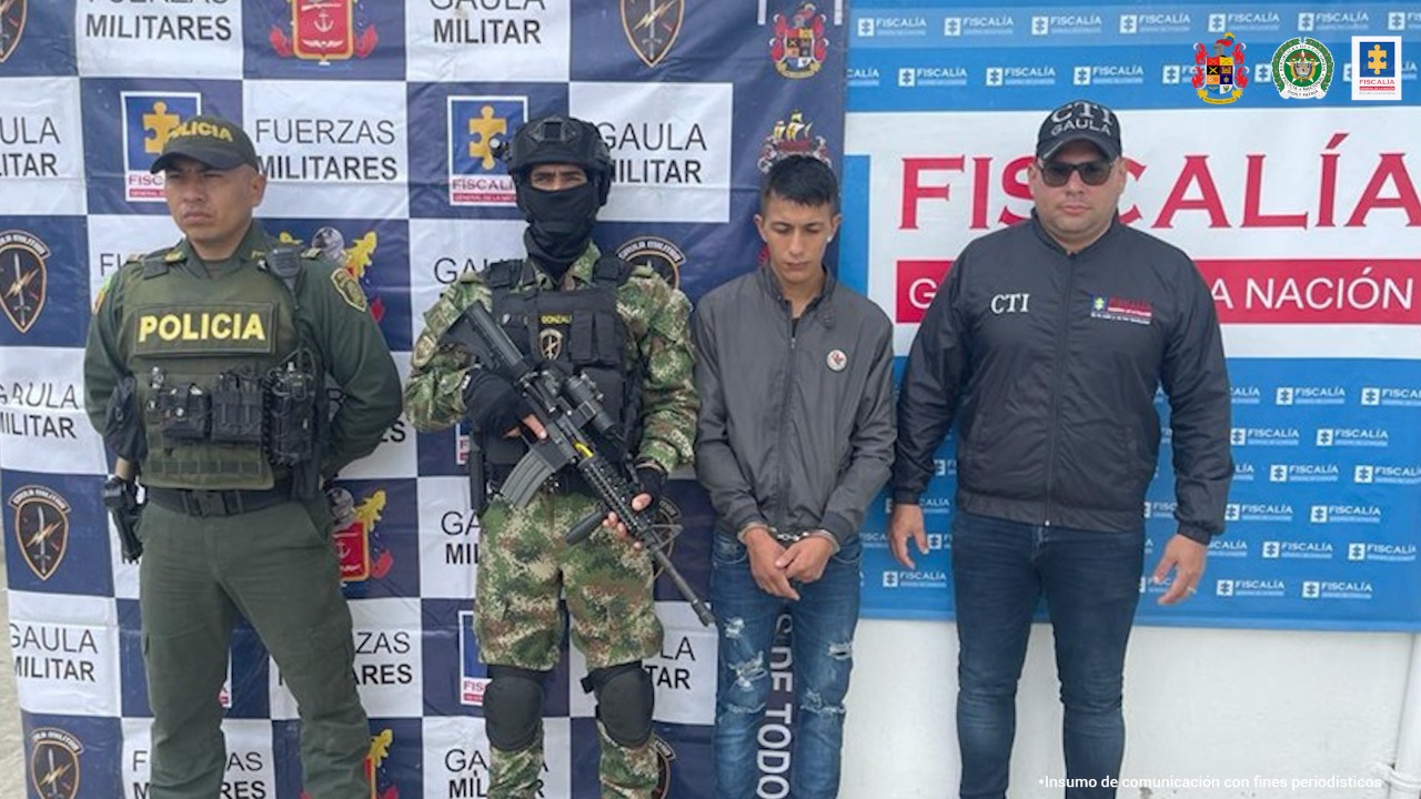 En la fotografía aparece un capturado, junto a personal de Policía Nacional, Ejército Nacional y Fiscalía General de la Nación. En la parte posterior de la imagen se ven banners de Ejército Nacional, Policía Nacional y la Fiscalía General de la Nación.