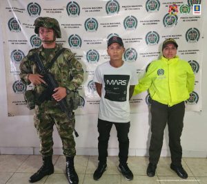 En la fotografía aparece un capturado, junto a personal de Ejército Nacional y Policía Nacional. En la parte posterior de la imagen se ven banners de Ejército Nacional, Policía Nacional y la Fiscalía General de la Nación.