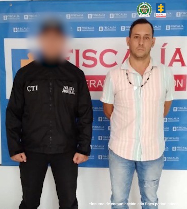 En la fotografía se aprecia de pie, con los brazos atrás a Cristian Camilo Ramírez González. Viste camisa de manga corta con rayas verticales color pastel rosado y azul; jean azul desteñido a la altura de los muslos y botas negras. Al lado derecho de él hay un servidor del CTI de la Fiscalía. Detrás de ellos hay un pendón institucional de la Fiscalía.