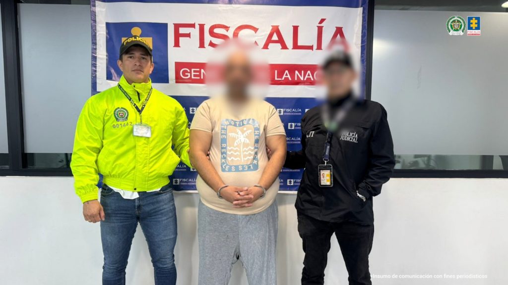 Se visualiza al capturado con el rostro difuminado junto a un investigador del CTI y un uniformado de la Policía Nacional. Detrás de ellos el banner que identifica a la Policía Nacional.
