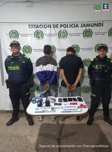 En la fotografía se aprecia de pie, con los brazos atrás, esposados y de espaldas a la cámara  a David Delgado Londoño y Wilfredo José Suárez Herrera. Uno viste buso de colores verde, blanco y azul; así como jean azul desgastado. El otro vista camisa negra de manga corta y pantalón de color gris. A los extremos de ellos hay uniformados de la Policía Nacional. Delante de ellos hay una mesa y sobre ella hay elementos como diademas, celulares,entre otros. Detrás de ellos hay un pendón institucional de la Policía.