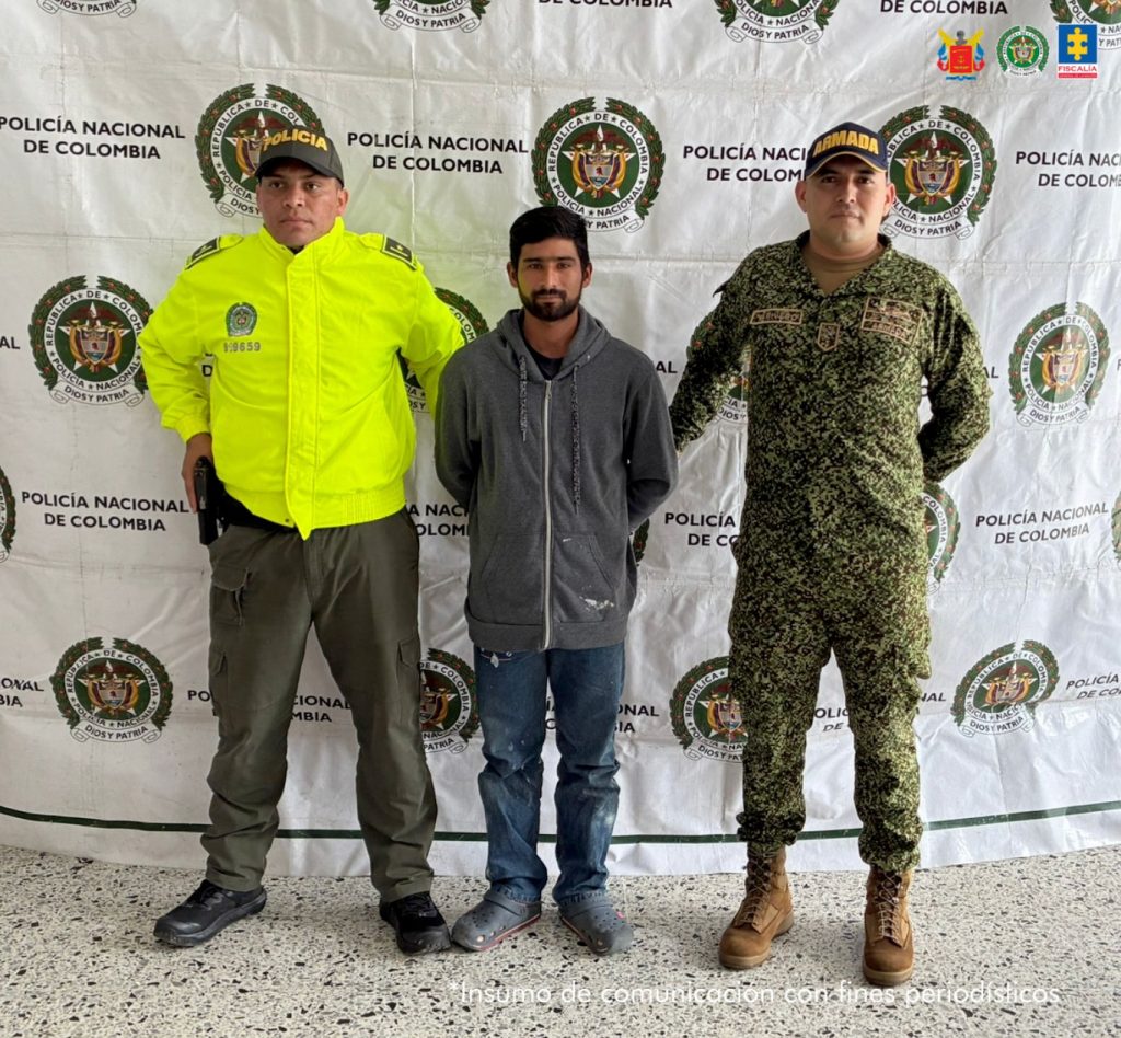 Se visualiza al capturado junto a dos uniformados de la Policía Nacional. En la parte posterior se ubica el banner de la Policía Nacional.