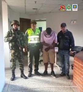 En la foto aparece en un pasillo, de pie, con los brazos adelante esposados y con la cabeza agachada, David Ortega Velasco. Viste camisa de color rosa, pantaloneta clara y zapatos oscuros. Al lado derecho de él hay un uniformado de la Policía y otro del Ejército. Al lado izquierdo hay un servidor del CTI de la Fiscalía.