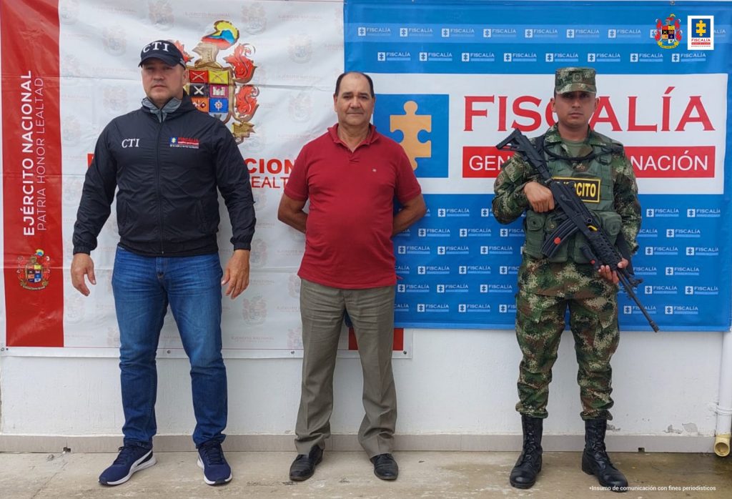 En la fotografía aparece un capturado, junto a personal de Fiscalía General de la Nación y Ejército Nacional. En la parte posterior de la imagen se ven banners de Ejército Nacional y la Fiscalía General de la Nación.    