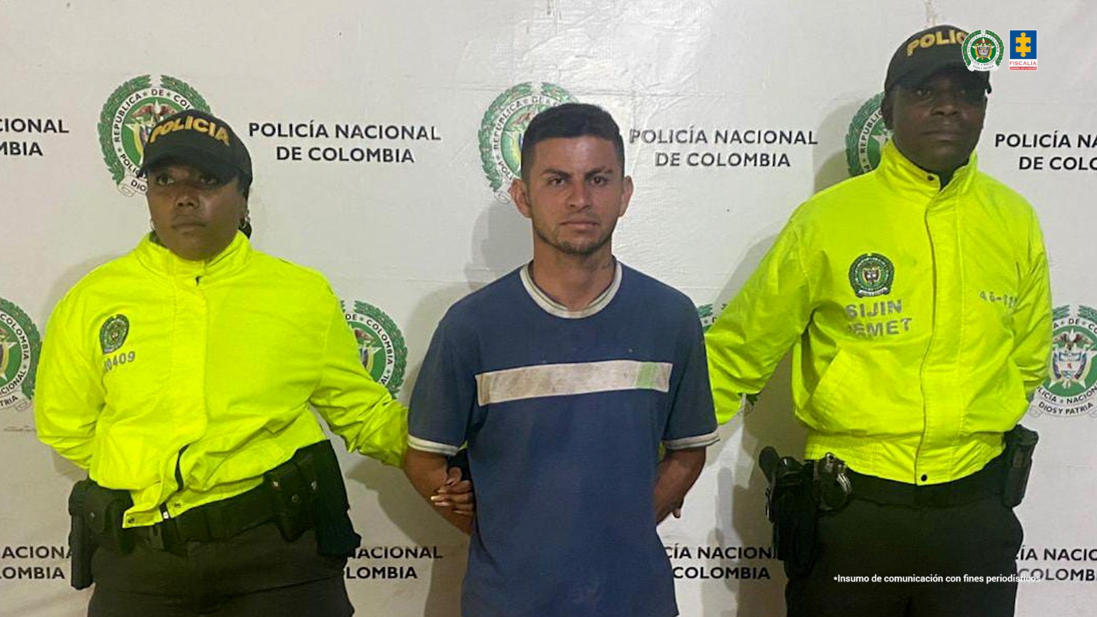 En la fotografía se aprecia de pie y con los brazos atrás a Davis Santiago Yela. Viste camiseta de manga corta, azul con franja blanca horizontal a la altura del pecho. A sus extremos hay uniformados de la Policía Nacional y detrás de ellos hay un pendón institucional de la Policía.