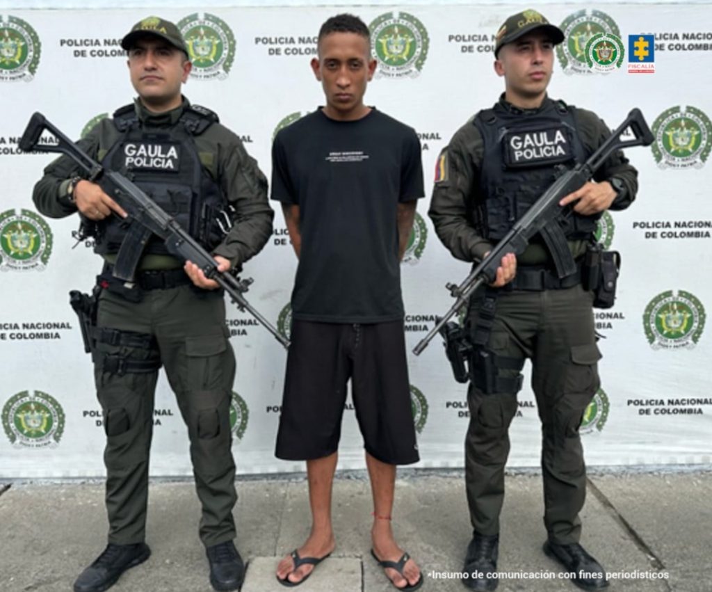 En la fotografía se aprecia de pie y con los brazos atrás a Deduin Giovanni Ceballos Triviño, alias Tata. Viste camiseta, de manga corta, y pantaloneta de color negro; asimismo, pantuflas negras. A sus extremos hay uniformados de la Policía Nacional. Detrás de ellos hay un pendón institucional de la Policía.