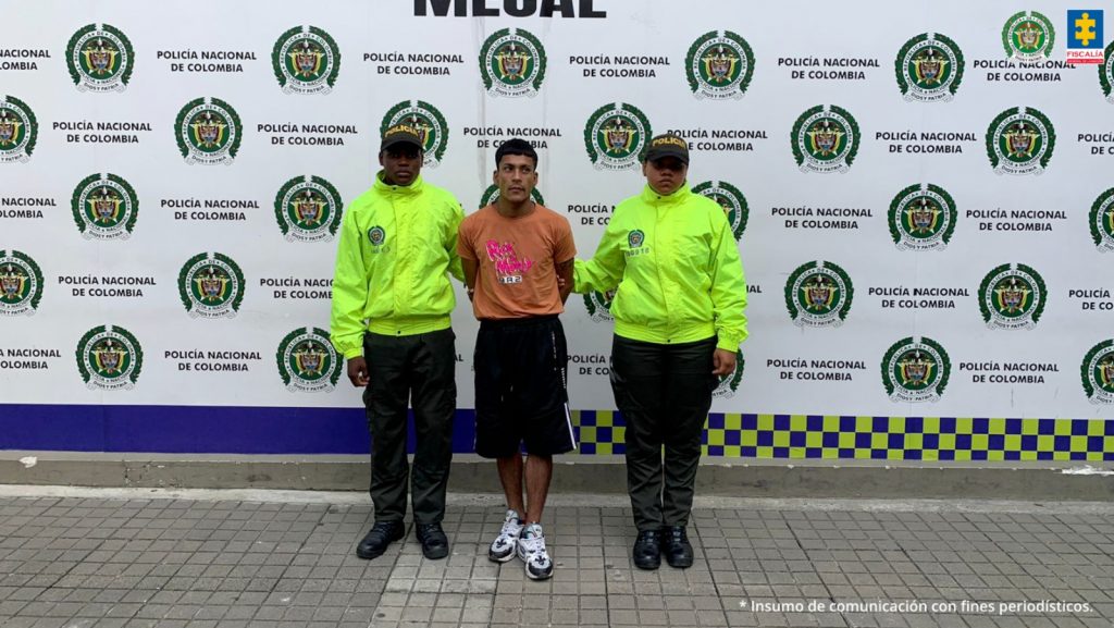 En la fotografía se aprecia de pie y con los brazos atrás a Deiber Alejandro Balcázar Beca. Viste camiseta de manga corta color naranja con estampado en el pecho color fucsia; bermuda negra y zapatillas blancas con negro. A lado y lado de él hay uniformados de la Policía Nacional. Detrás de ellos hay  un pendón institucional de la Policía.
