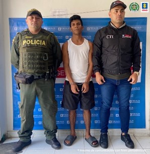 En la imagen se observa el capturado junto a un investigador del CTI y un uniformado de la Policía Nacional. En la parte posterior se observa el banner de la Fiscalía General de la Nación.