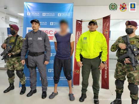 En la imagen se aprecia el capturado junto a un investigador del CTI y uniformado de la Policía y Ejército Nacional. En la parte posterior se observa los banners que identifican a la Fiscalía General de la Nación y al Ejército Nacional.