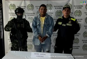En la imagen aparece una persona de camiseta amarilla, jean y camisa de jean, entre dos uniformados de la Policía Nacional. 