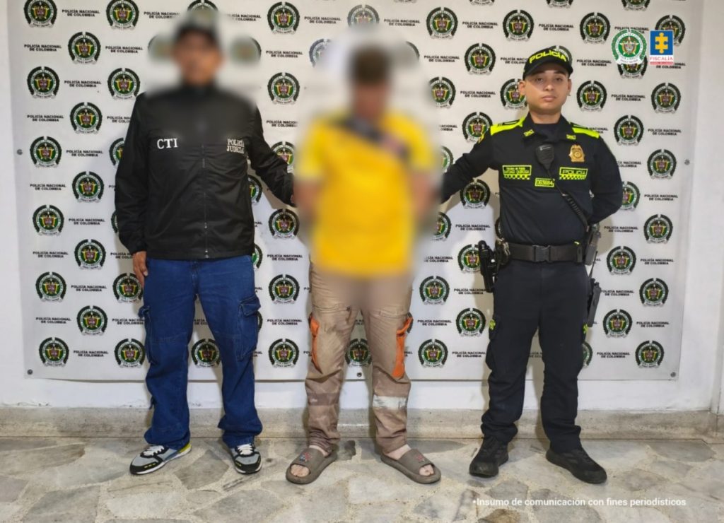 En la foto se observa al agresor en custodia por un servidor del CTI y un uniformado de la Policía Nacional. Detrás hay un backing de la Policía Nacional.