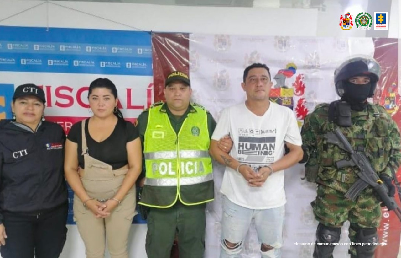 En la fotografía aparecen 2 personas capturadas, un hombre y una mujer, junto a una funcionaria del CTI, la Policía Nacional y el Ejército. En la parte posterior se ven un banner de la Fiscalía y del Ejército.