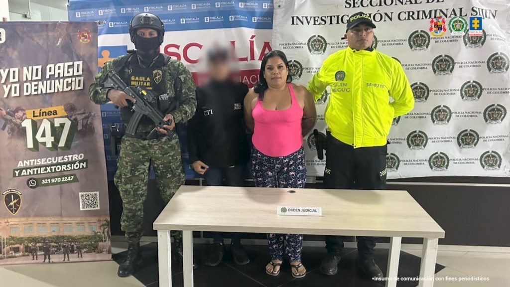 Se observa a la capturada junto a una investigadora del CTI y uniformados de la Policía y Gaula Militar. Detrás de ellos los banners institucionales del Gaula Militar, Fiscalía General de la Nación y Policía Nacional
