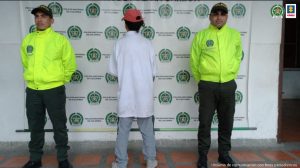 en la imagen se ve una persona detenida de espaldas, bajo custodia de dos integrantes de la Policía Nacional. Detrás de los uniformados un backing institucional.