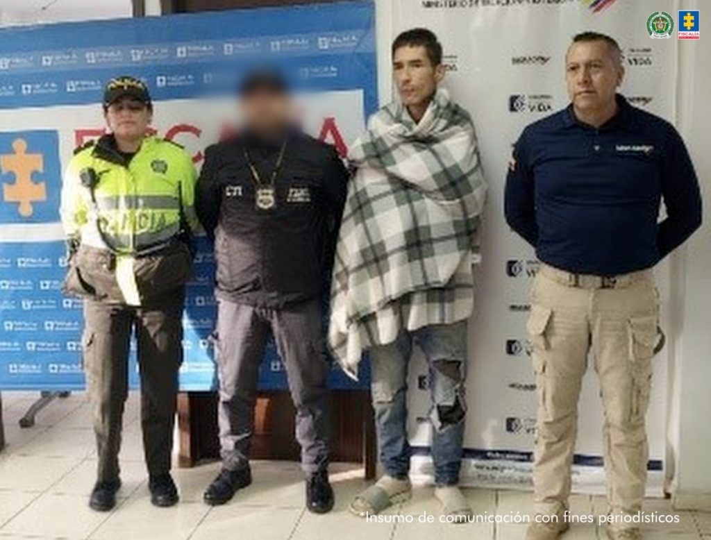 En la fotografía aparece de pie y abrigado con una manta de cuadros grises y blancos, Diego Armando Guzmán. Viste con jean azul desgastado y pantuflas. Al extremo derecho hay un servidor del CTI de la Fiscalía y de la Policía Nacional. Al extremo izquierdo un servidor de Migración Colombia. Detrás de ellos hay dos pendones institucionales de la Policía y de Migración Colombia.