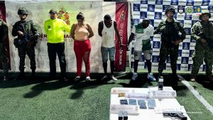 En la fotografía aparecen los capturados junto a un agente de la Policía Nacional y cuatro infantes de la Armada Nacional. En la parte posterior está una mesa con un arma, municiones, teléfonos celulares, un computador y un escáner satelital