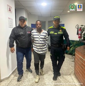 En la fotografía se aprecia en acción de caminata a Duván Estiven Guevara Meza. Viste camibuso de manga larga con rayas grises y blancas; pantalón oscuro y tenis blancos. Al lado derecho de él hay un servidor del CTI y al lado izquierdo un uniformado de la Policía Nacional.