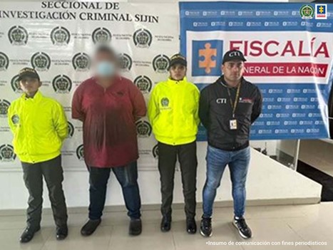 En la fotografía aparece un hombre capturado junto a personal de la Policía Nacional y del CTI. En la parte posterior se ve un banner de la Policía Nacional-SIJIN y de Fiscalía General de la Nación.
